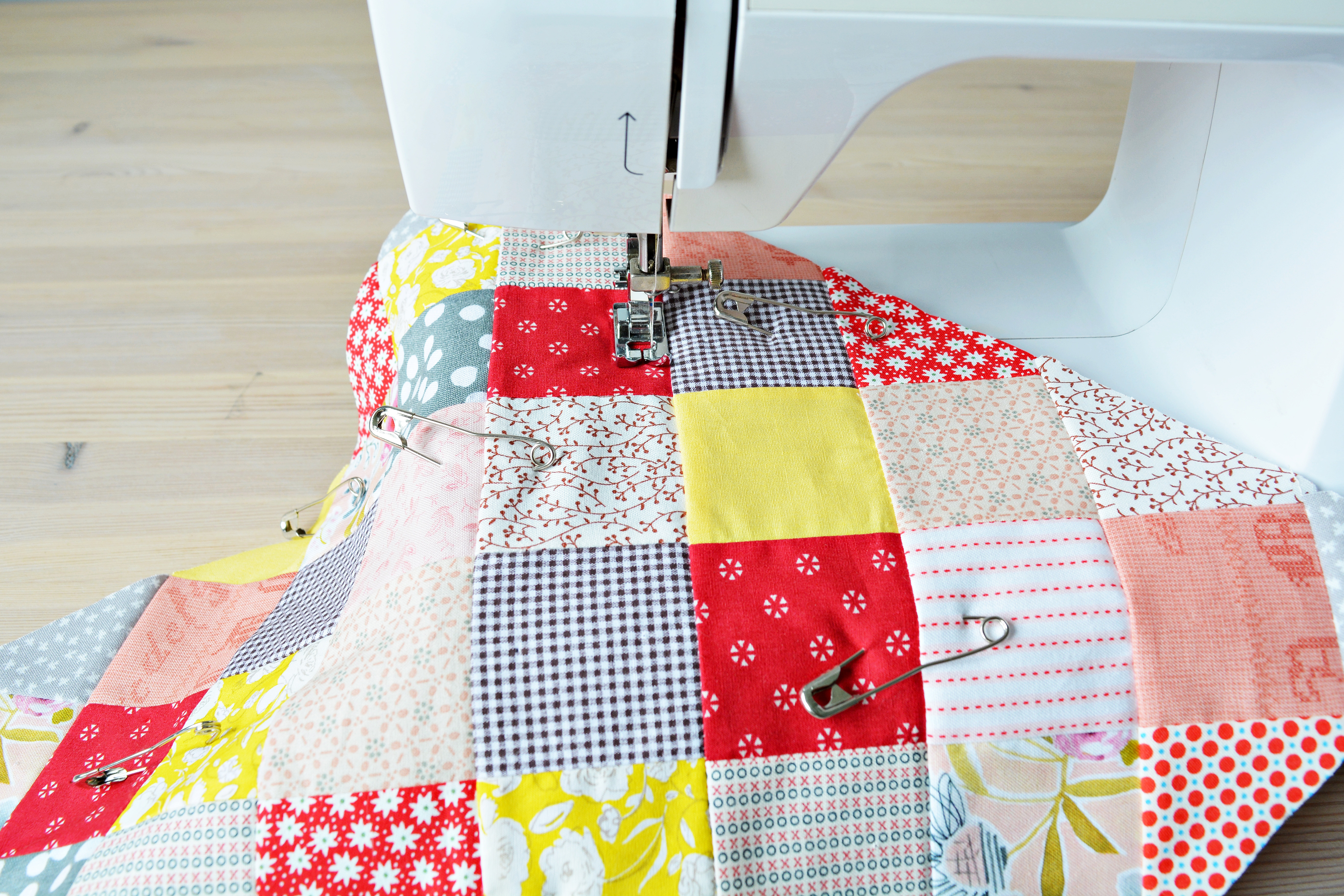 Working process: quilt, metal pins and sewing machine on wooden table