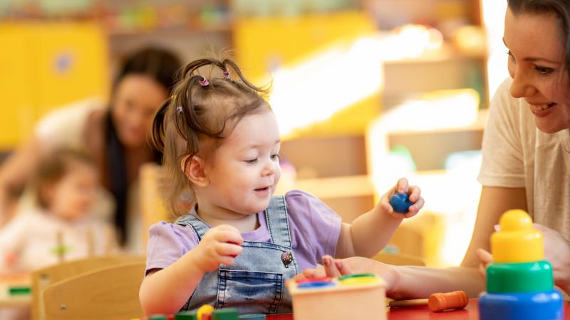 Babies with teachers playing with developmental toys in nursery